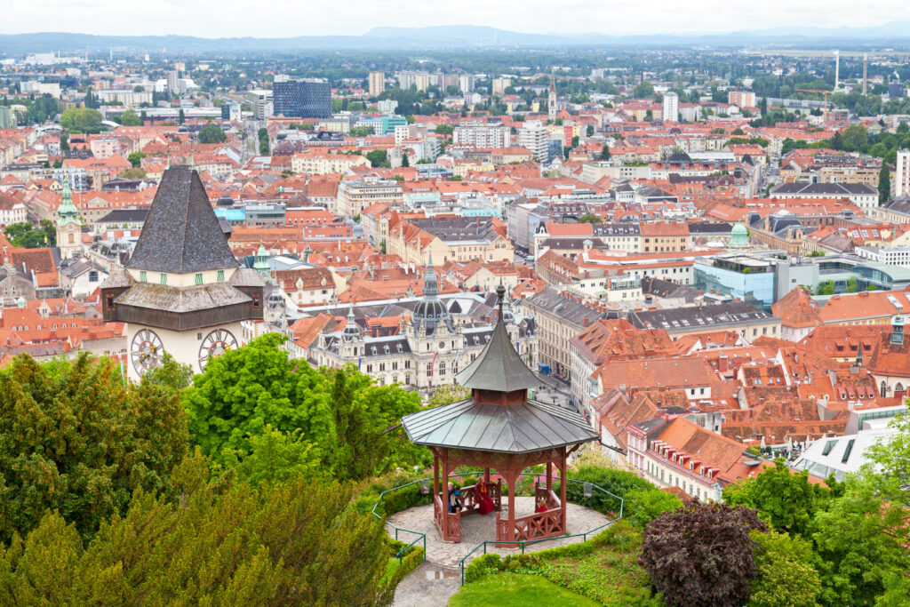 Graz, Austria - May 28 2019: Aerial view of Graz with people seat inside the Chinese Pavilion (Chinesischer Pavilion) next to the Clock Tower (Uhrturm).